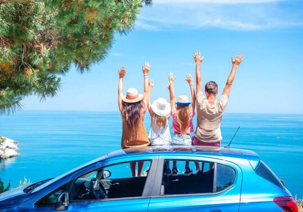Family sitting on car with hands up for summer vacation.