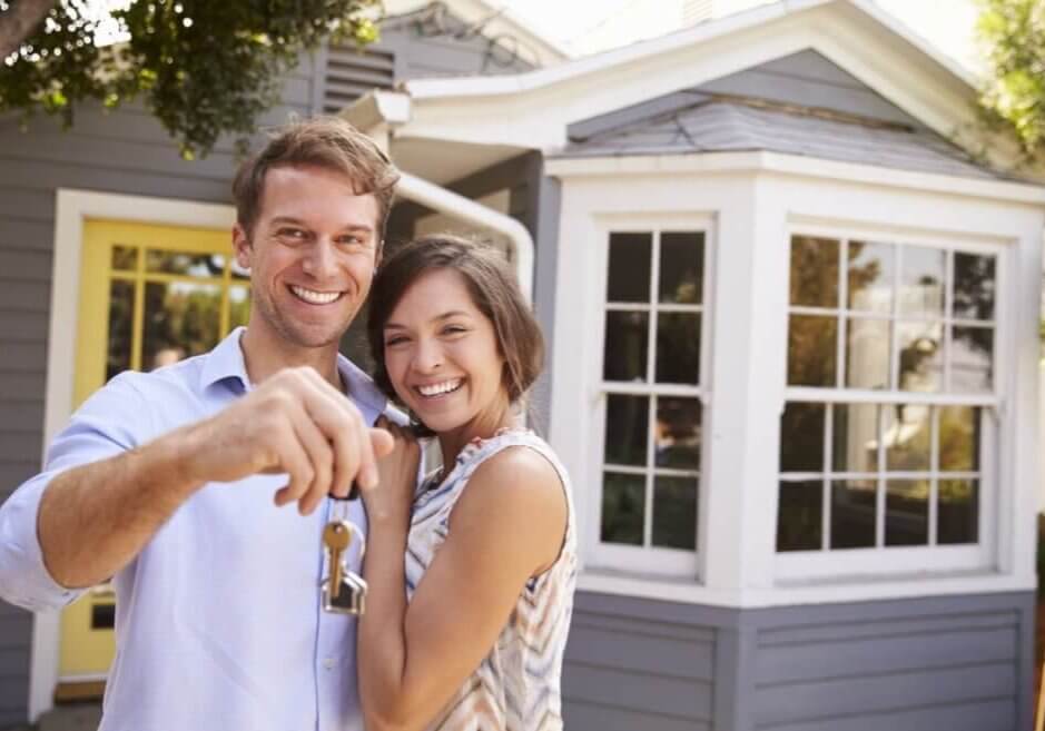 Couple with keys standing outside new home.